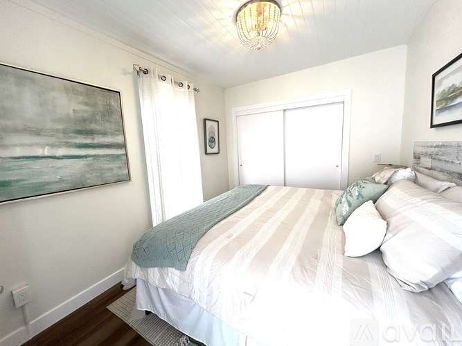 A bedroom with a bed, a painting, and a window.