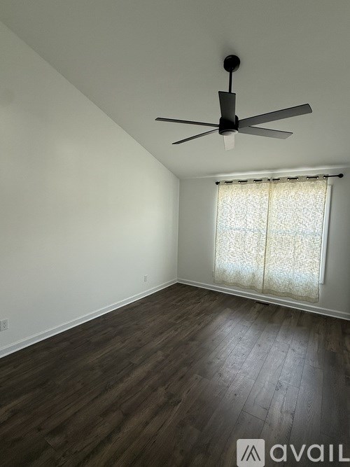A room with a ceiling fan and a window with curtains.