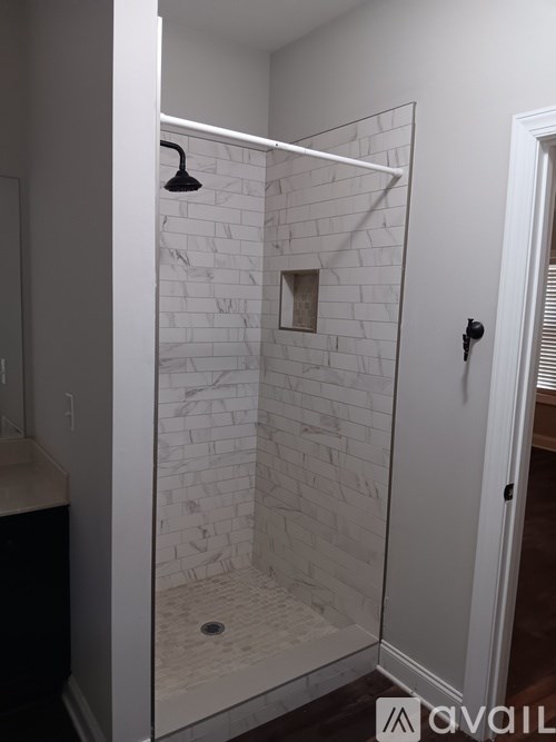 A white tiled shower with a black shower head.
