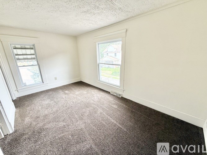 A room with a carpeted floor and two windows.