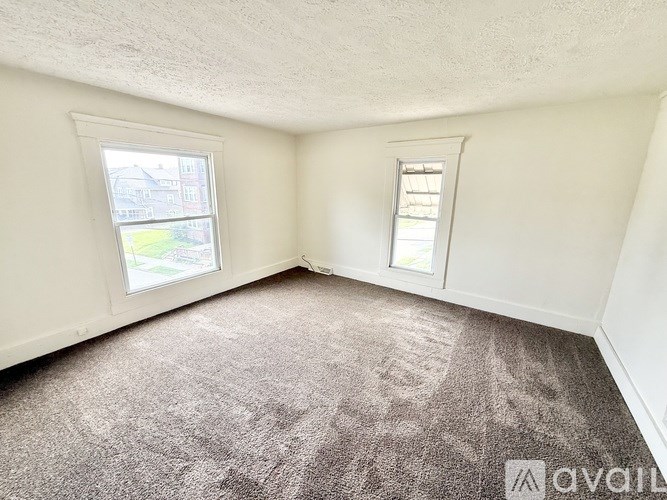 A room with a carpeted floor and two windows.
