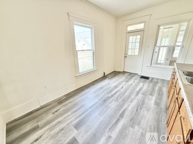 A spacious room with wooden flooring and white walls.