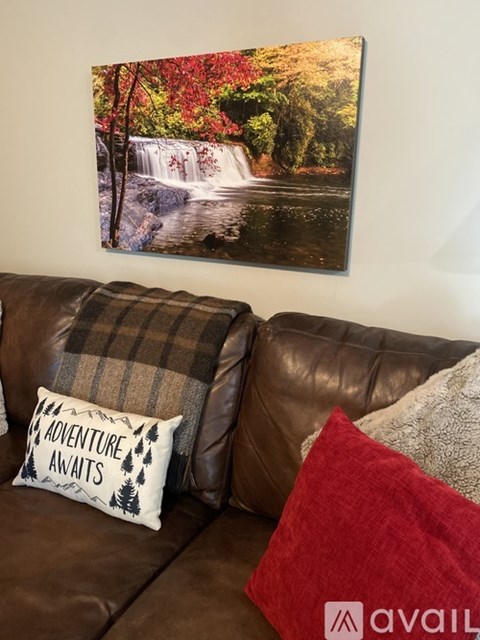 A brown leather couch with a pillow that says "Adventure Awaits" and a red pillow on it.