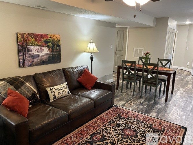 A living room with a brown leather couch and a painting of a waterfall on the wall.