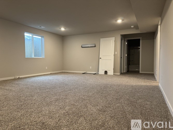 A room with a carpeted floor, a window, and a door leading to another room.