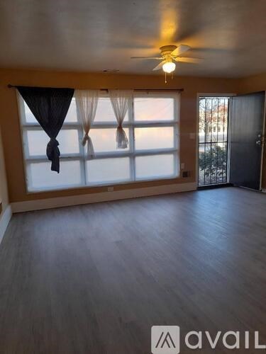 A room with a ceiling fan and a large window with curtains.