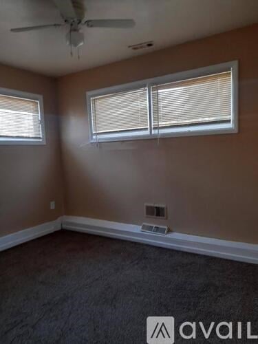 A room with a ceiling fan and two windows.