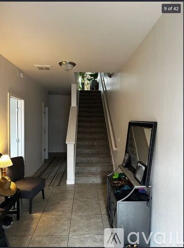 A hallway with a staircase, a chair, a mirror, and a cabinet.