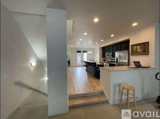 A modern kitchen with a bar stool and a laptop on the counter.