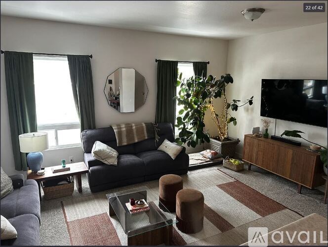 A living room with a black couch, a glass coffee table, and a flat-screen TV mounted on the wall.