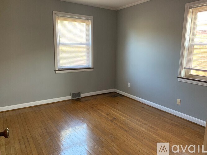 A room with wooden flooring and two windows.