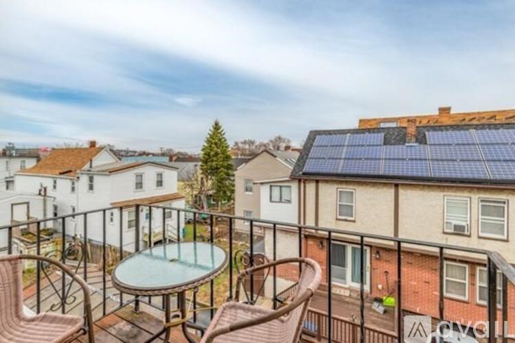 A balcony with a table and chairs overlooks a courtyard with a tree and a building with solar panels.