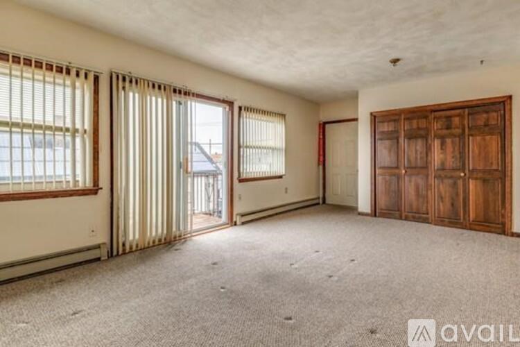 A room with a carpeted floor, a wooden door, and a window with blinds.