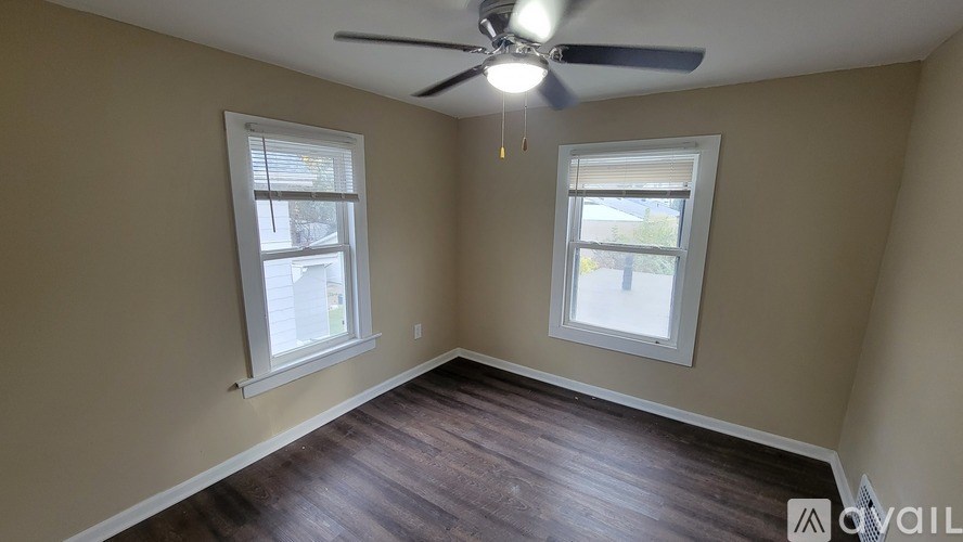 A room with a ceiling fan and two windows.