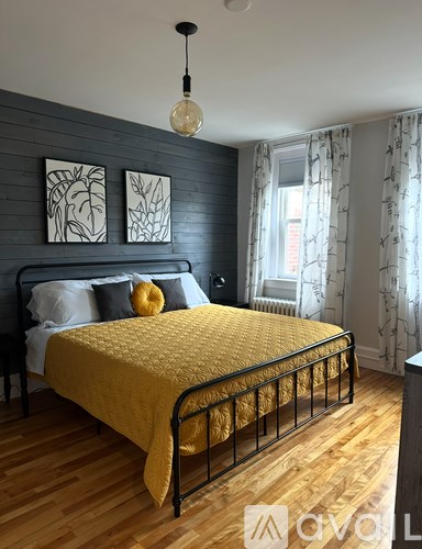 A bed with a yellow cover and a black metal frame in a room with wooden flooring.