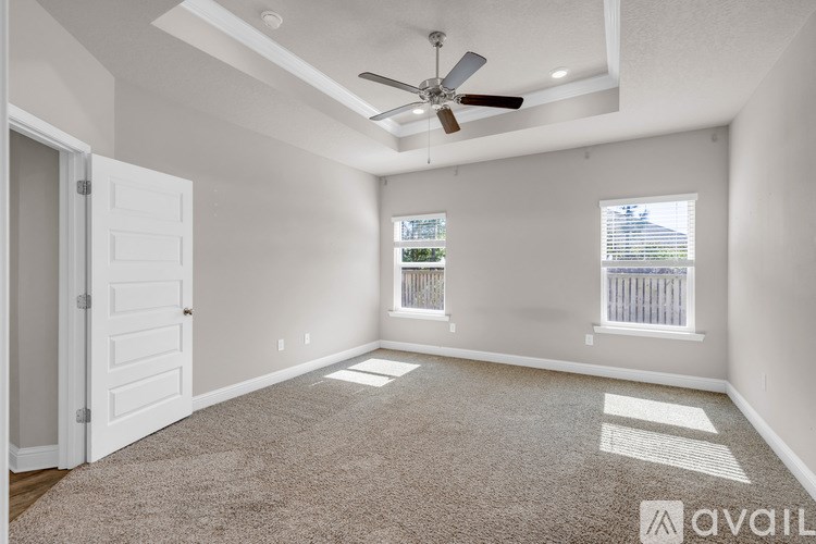 A room with a carpeted floor, a ceiling fan, and a window with blinds.
