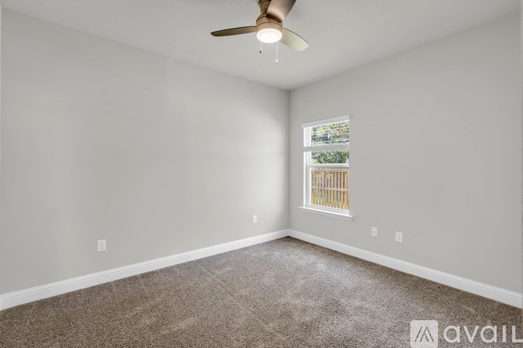 A room with a ceiling fan and a window with a view of trees and a fence.