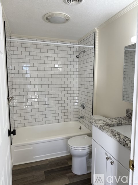 A white toilet sits in a bathroom with a white bathtub and a white tiled shower.