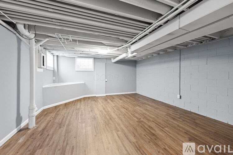 A spacious room with wooden flooring and white walls, featuring exposed pipes on the ceiling.