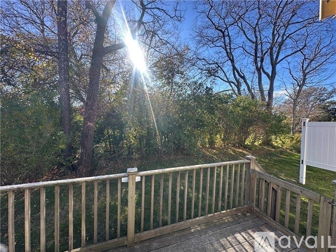 A deck with a railing and a view of trees and a white fence.