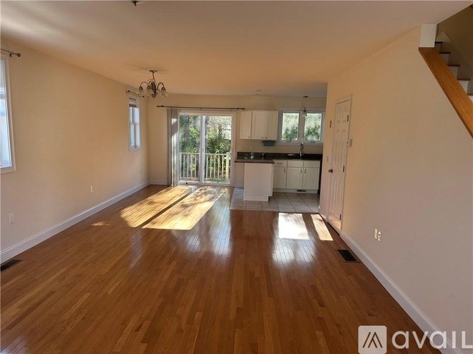 A spacious room with wooden floors and a staircase on the right side.