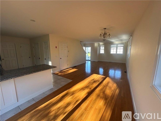 A sunlit kitchen and living room with wooden floors and white walls.