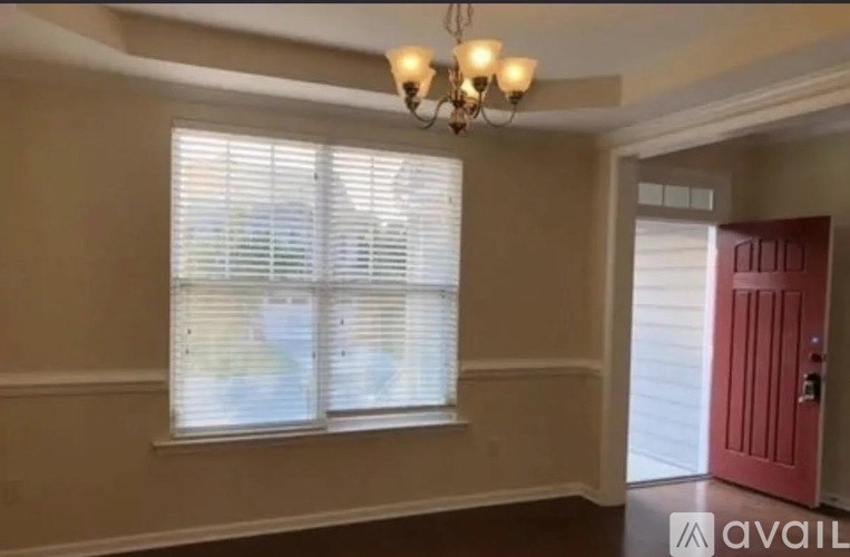 A room with a window covered by white blinds and a chandelier hanging from the ceiling.