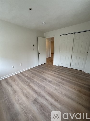 A room with wooden flooring and white walls, with a doorway leading to another room.