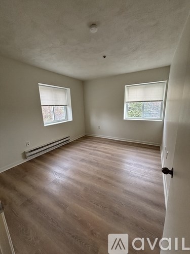 A room with wooden flooring and two windows.
