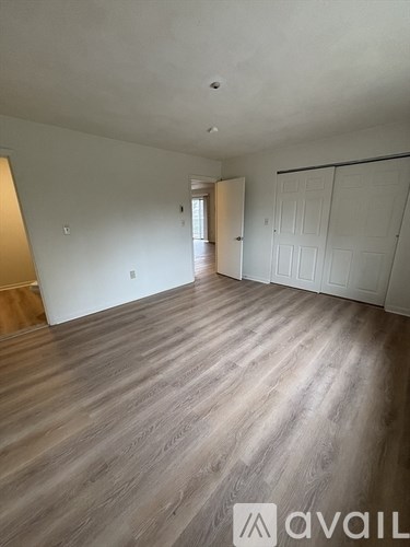 A room with wooden flooring and white walls, with a door on the right side.