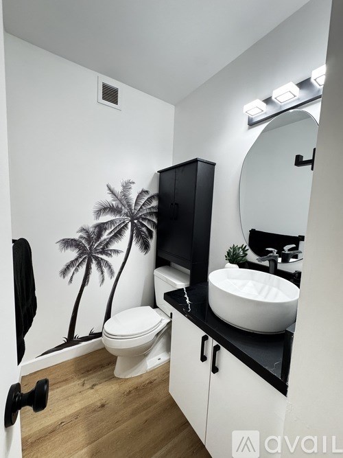 A bathroom with a toilet, sink, and a wall decal of a palm tree.