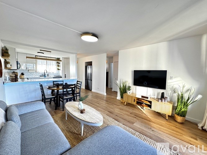 A living room with a grey sofa, a coffee table, a dining table with chairs, a television, and a potted plant.