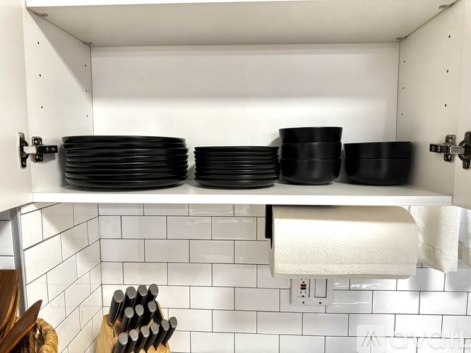 A kitchen cabinet with black plates and a roll of paper towels.
