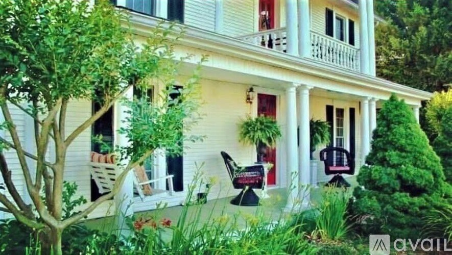 A white house with a balcony and a tree in front.