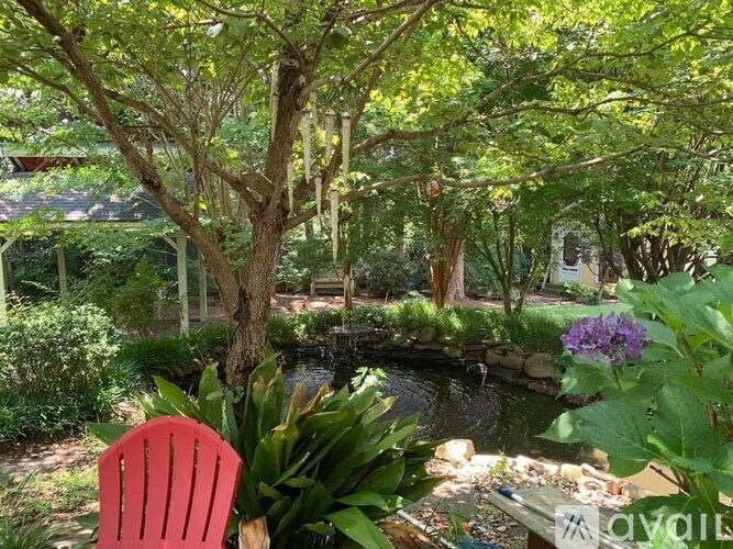 A red chair is in the foreground of a lush garden with a pond.