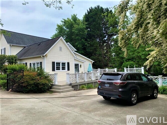 A car is parked in front of a white house with a black roof.