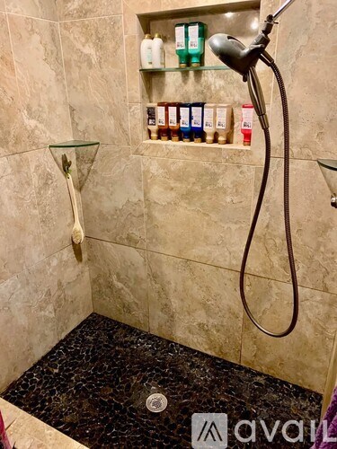 A bathroom with a shower head and a shelf with toiletries.