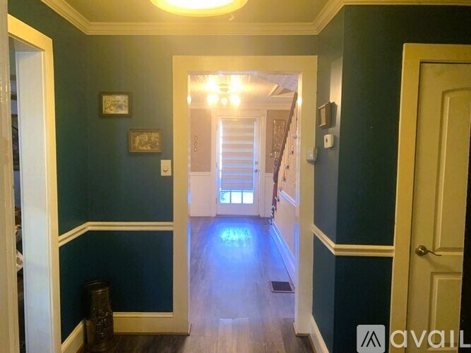 A hallway with a wooden floor and a staircase in the background.