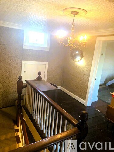 A chandelier hangs over a staircase with a wooden banister.
