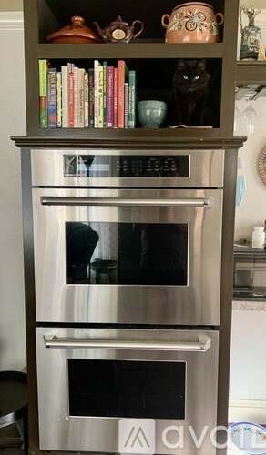 A double oven built into a cabinet with a shelf above it.