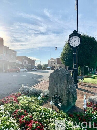 A clock on a pole stands in front of a large rock with a plaque that reads "EST. 1940".