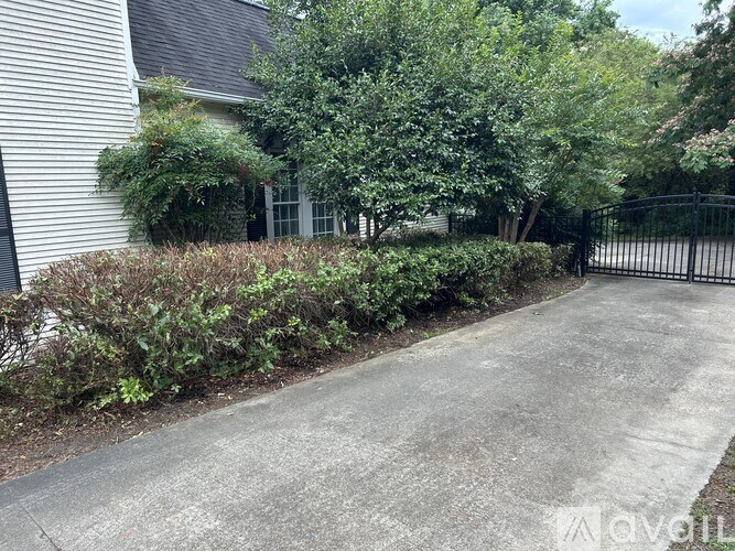 A driveway leads to a house with a black fence and green trees.