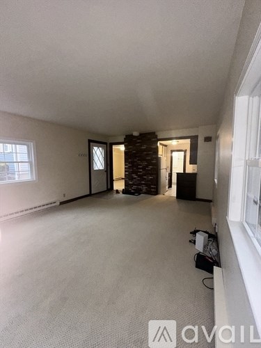 A spacious room with a carpeted floor and a window on the left side.