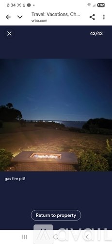 A nighttime view of a property with a lit pathway leading to a gas fire pit.