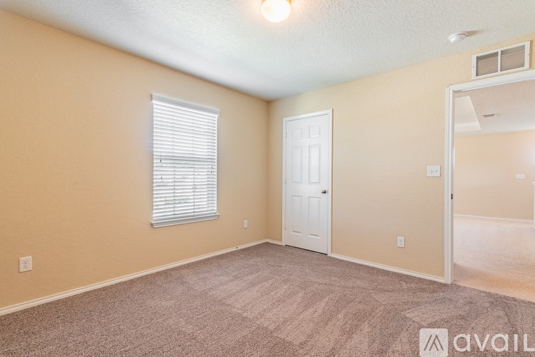 A room with beige walls, carpeted floor, a window with blinds, a door, and a mirror on the wall.