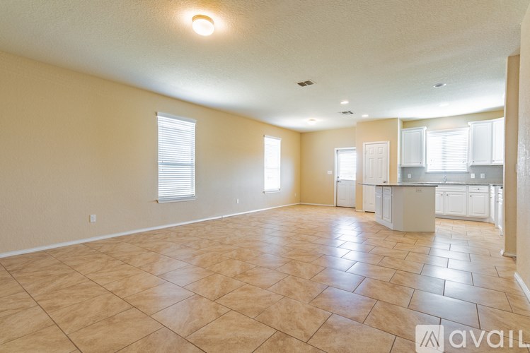 A spacious room with tile flooring and a kitchen area in the background.