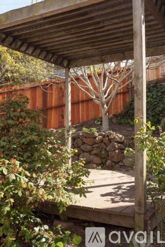 A wooden pergola with a stone wall and a tree in the background.