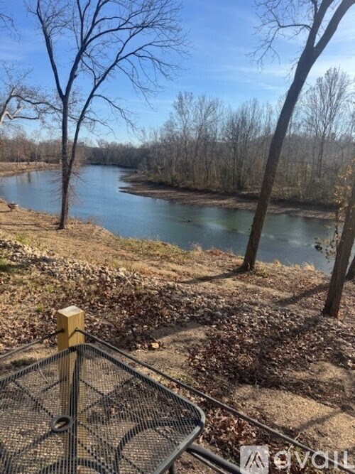 A river flows through a wooded area with a fence in the foreground.