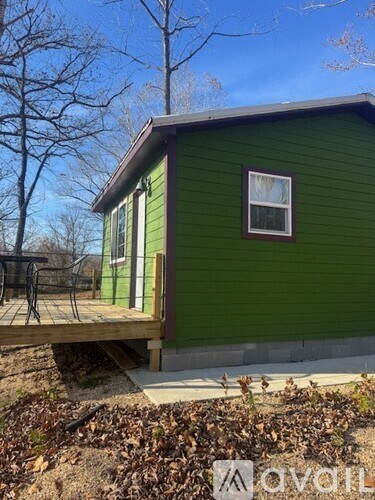 A green house with a deck and a tree in the background.