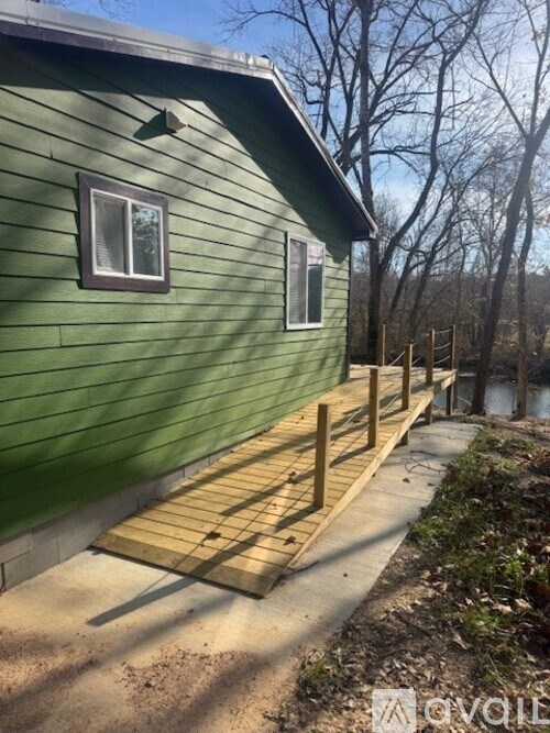 A green house with a wooden deck and a river in the background.